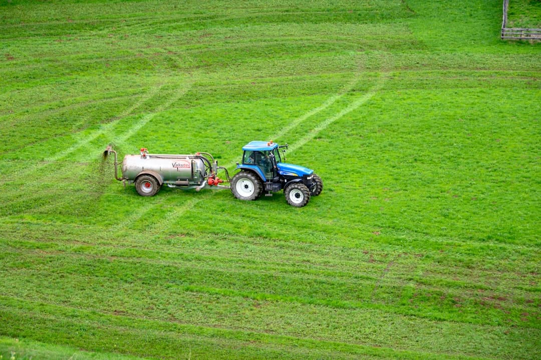 Traktor med tankvagn arbetar på en grön äng vid Vättern.
